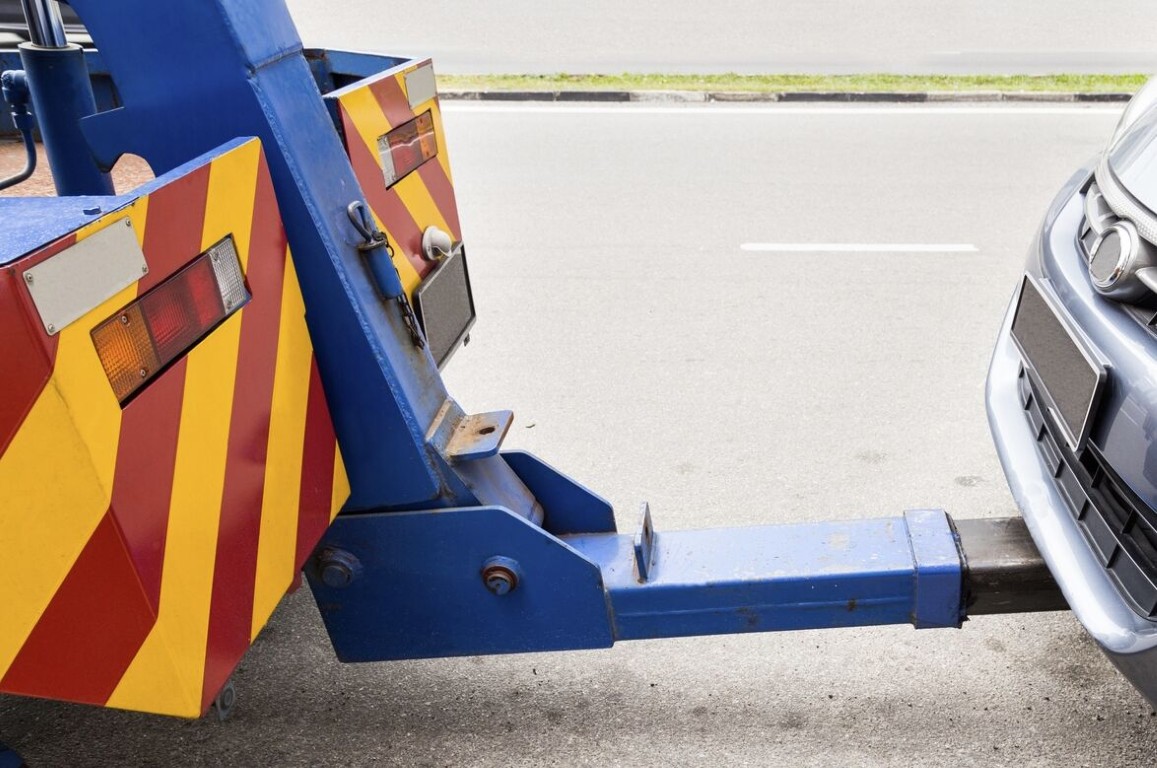 Tow truck hookup arm connecting to a car bumper for battery replacement service in Cardiff, CA