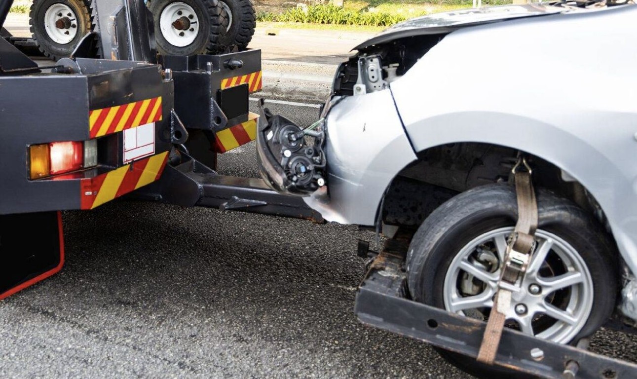 Roadside assistance tow truck lifting a damaged silver car on the highway