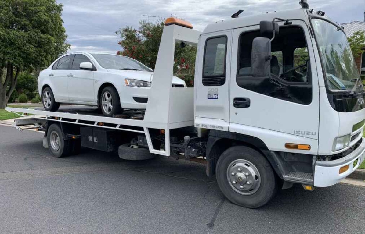 White Isuzu flatbed tow truck loading a vehicle for motorcycle towing service in Cardiff, CA