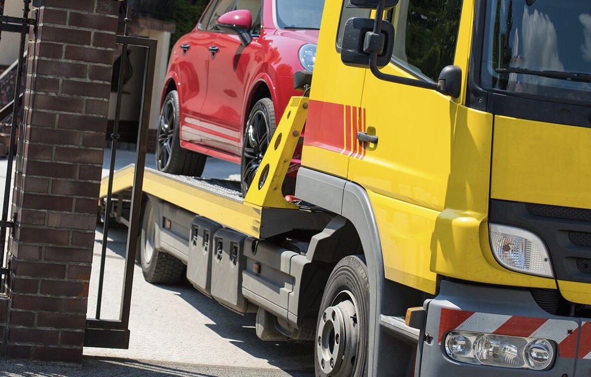 Yellow flatbed tow truck safely transporting a car near Solana Beach, CA